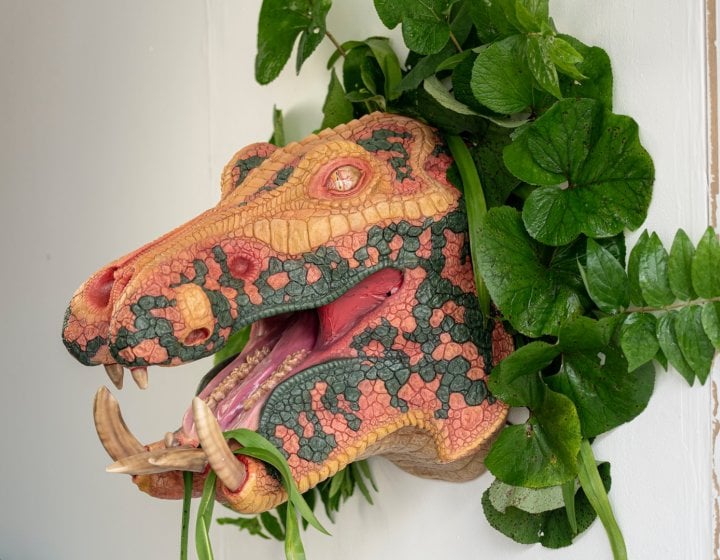 A multi-coloured velociraptor head is adorned with leafy green plants